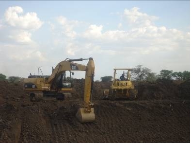 Excavator shaping the side slopes while as the bulldozer levels and trims the earth bund in Karamoja